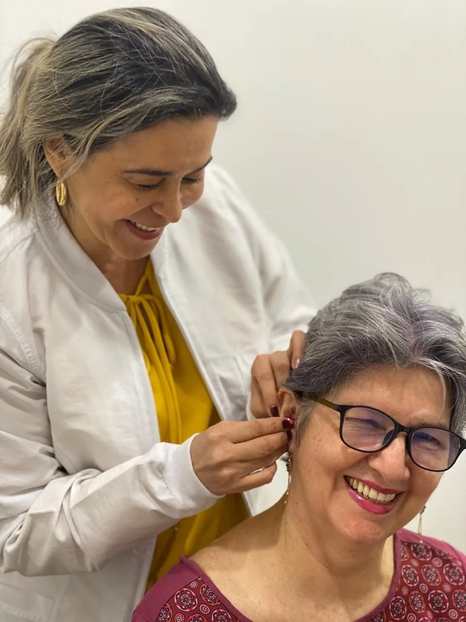 Especialista adaptando un audífono a una paciente que sonríe